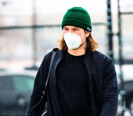 nolan patrick squints against the snowy sky, a green beanie on his head popping out of the photo against his black and grey clothes.